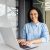Portrait of successful woman helpline worker, using headset phone for video call, smiling and looking at camera, indian woman happy with dream job, inside office with laptop.
